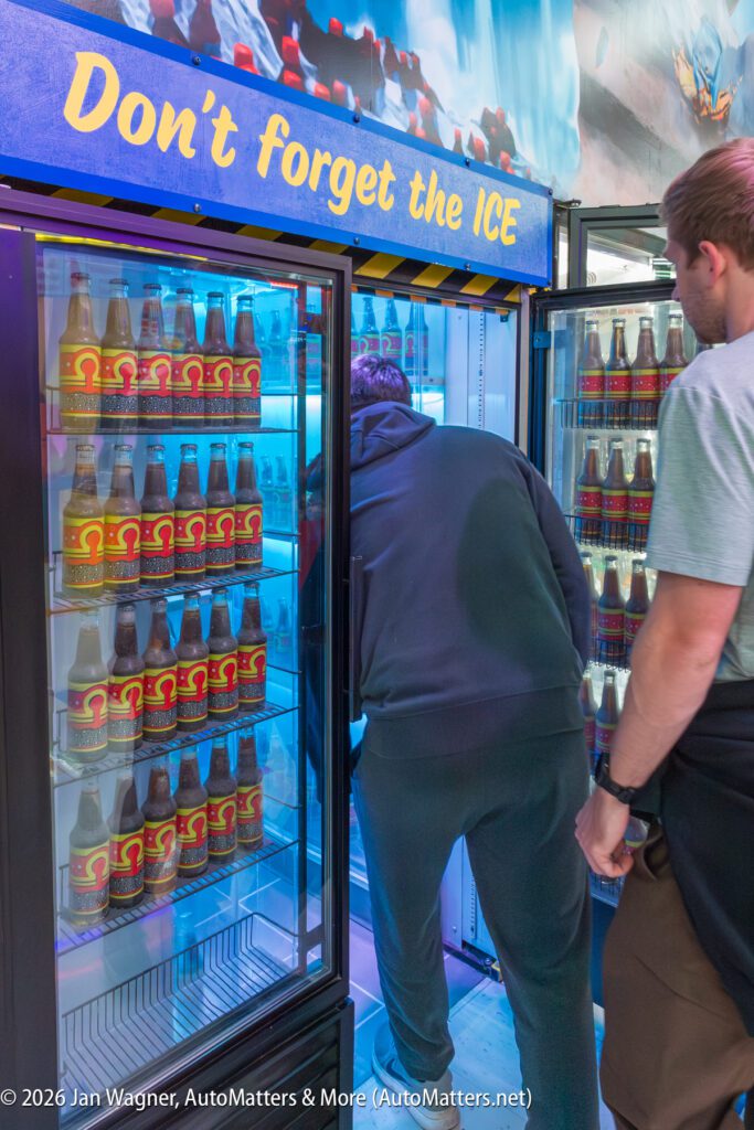 Two people stand at a cooler labeled "Don't forget the ICE," which contains bottles of soda on the left and a person reaching into an ice compartment on the right.