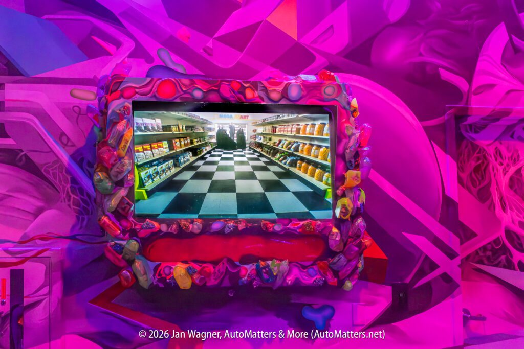 A television displaying a supermarket aisle is mounted on a colorful wall with purple, pink, and blue abstract designs and a decorative frame.