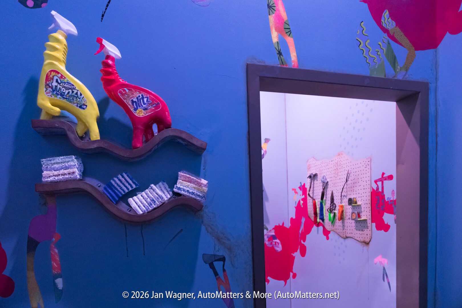 A blue wall with wavy shelves holding cleaning bottles and soap bars, next to a doorway showing a pegboard with tools hanging on it.