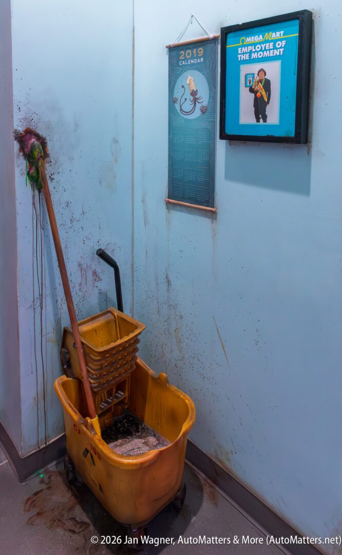 A dirty mop and yellow bucket are against a stained wall under a 2019 calendar and an "Employee of the Moment" plaque at OmegaMart.