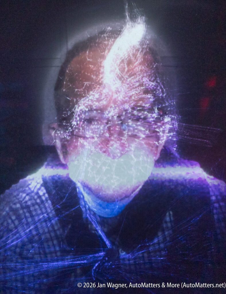 A person wearing glasses and a mask is illuminated by abstract, glowing light patterns in a dark setting.