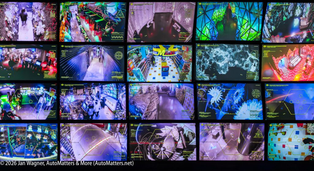 A large display wall shows multiple surveillance camera feeds from various locations, featuring interior spaces, objects, and graphics, each with overlaid data and interface elements.