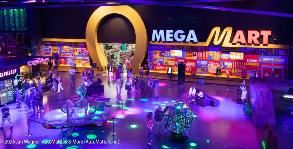 Wide view of a colorful, futuristic indoor mall with neon lights, people walking or sitting, and a large "MEGA MART" sign above an archway entrance.