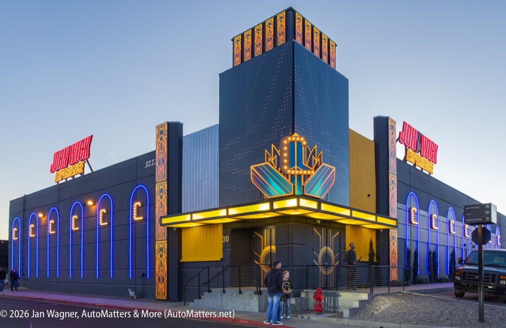 A modern building with neon blue and yellow lights, labeled “Johnny Rockets,” with people standing near the entrance at dusk.