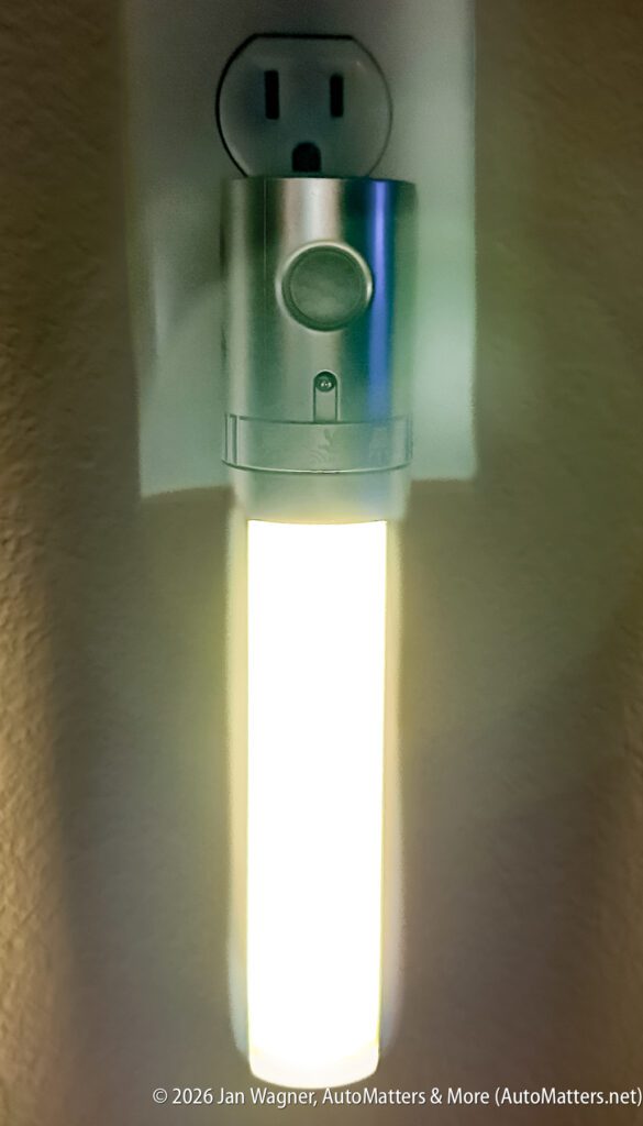 A plug-in night light is illuminated in a wall outlet, casting a soft glow against a beige wall.