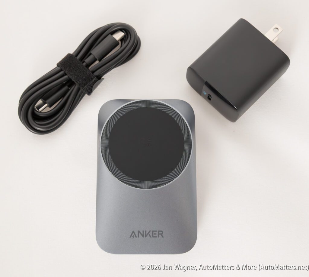 An Anker wireless charging pad, black power adapter, and USB-C charging cable with a Velcro strap are displayed on a white surface.