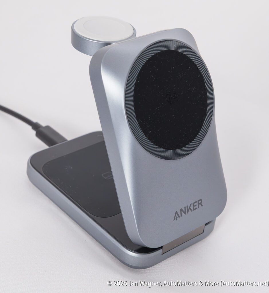 A silver and black Anker wireless charging stand with a circular charging pad and a foldable design, shown connected via a cable.