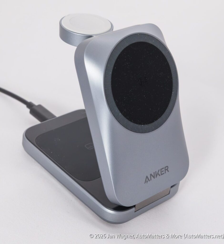 A silver Anker wireless charging stand with a circular charging pad and an additional charging spot on top, connected to a power cable on a white background.