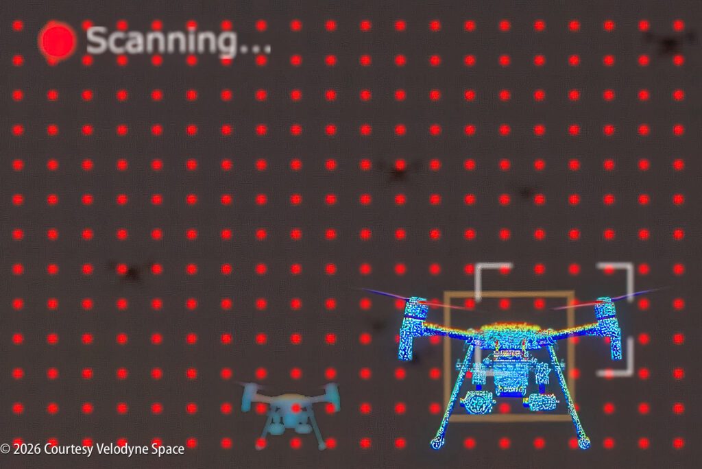 A digital graphic shows a 3D scan of two drones against a grid of red dots, with the word “Scanning…” and a red indicator in the upper left corner. ©2026 Courtesy Velodyne Space.