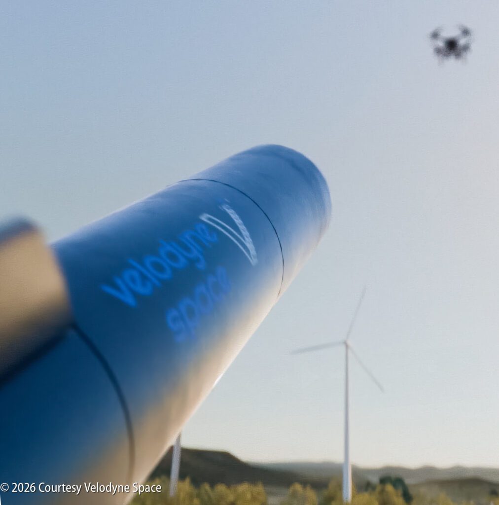 A blue Velodyne Space rocket is aimed at the sky; a wind turbine and a drone in flight are visible in the background.