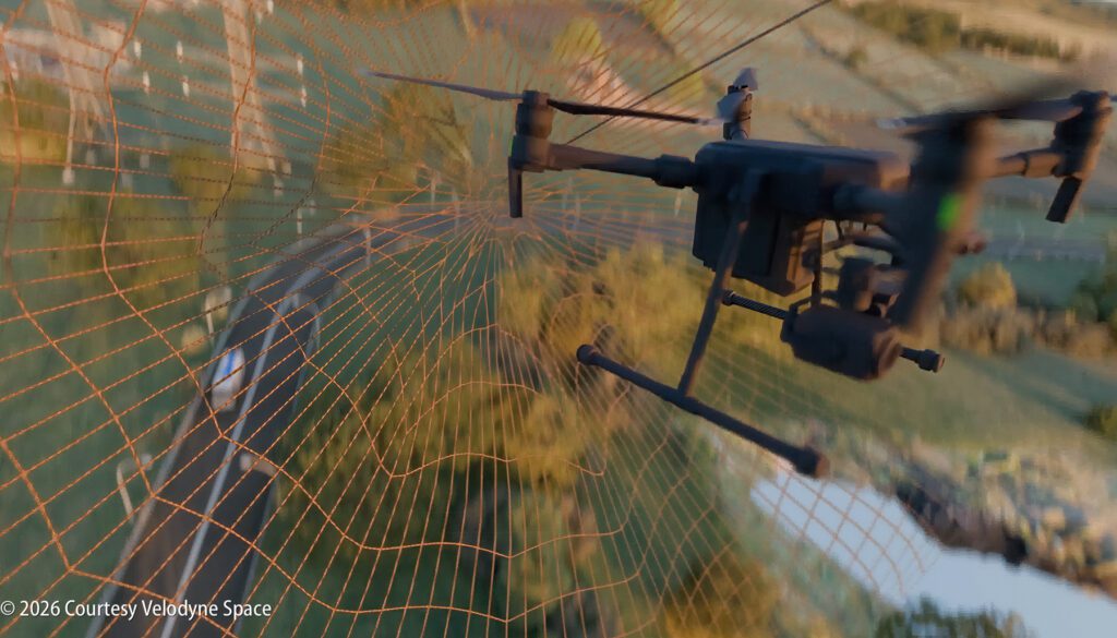 A drone caught in a large, orange net suspended outdoors over a rural landscape with trees and fields.