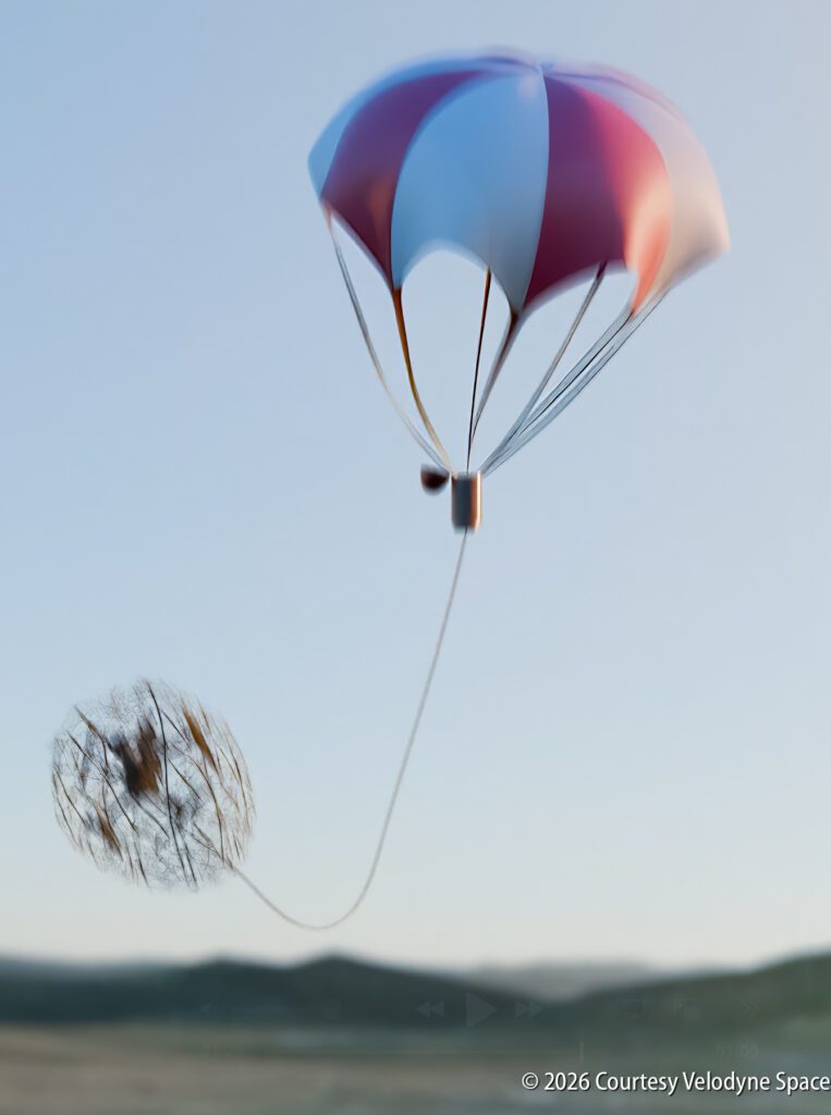 A capsule with a red, white, and blue parachute descends as a drogue chute trails behind, set against a clear sky and distant hills.