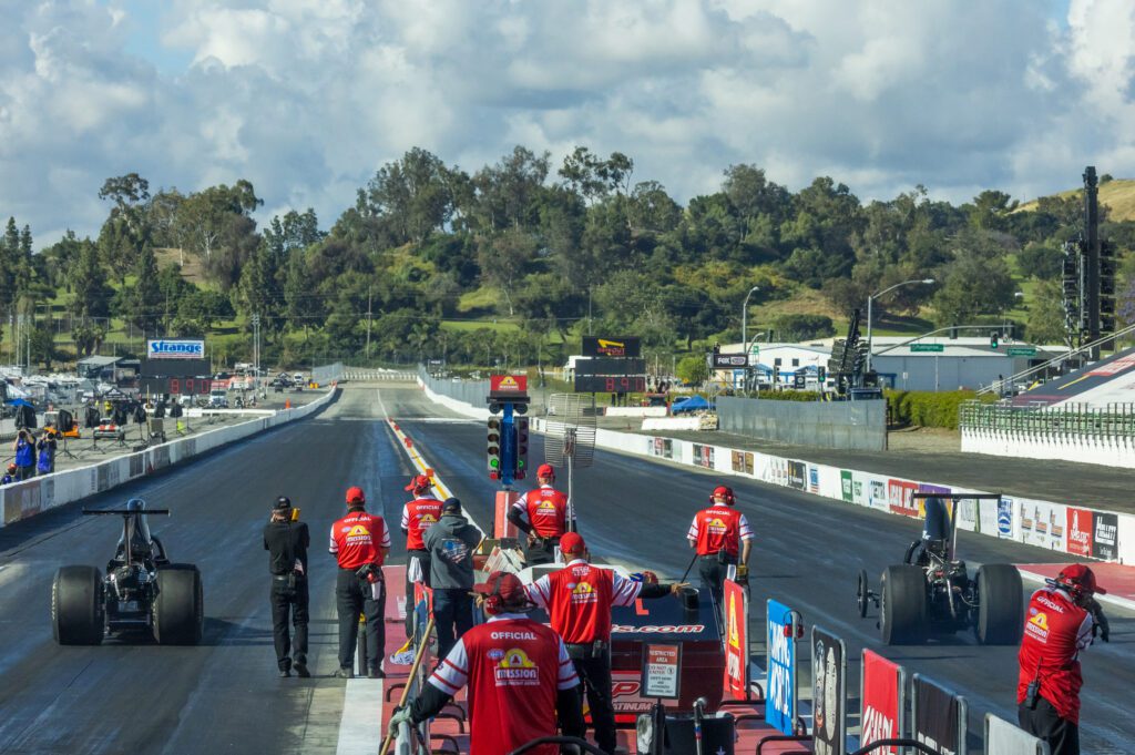 Drag racing event with officials in red shirts watching a dragster.