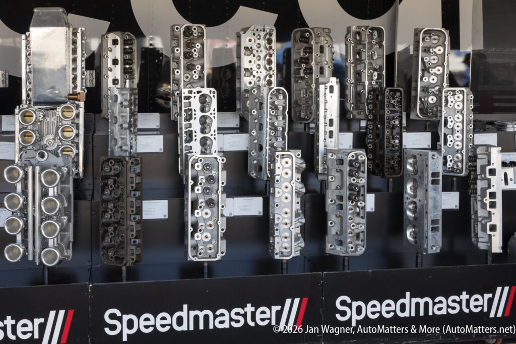 A display of multiple polished engine cylinder heads, arranged vertically on shelves, with the Speedmaster logo visible at the bottom.