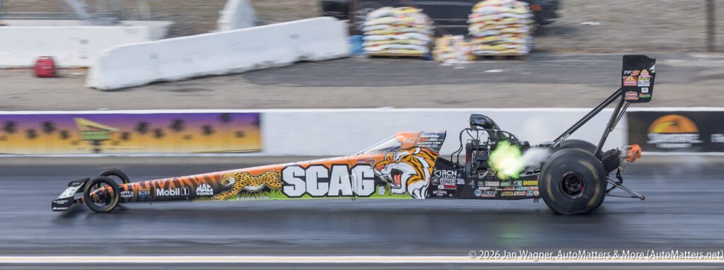 A dragster with a tiger-themed SCAG design speeds down a racetrack, emitting green flames from its exhaust.