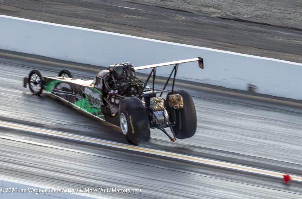 A dragster with its front wheels lifted off the ground accelerates down a drag strip during a race.