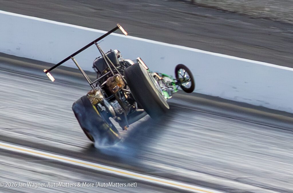 A drag racing car lifts off the ground on its rear wheels, with smoke coming from the tires on a racetrack.