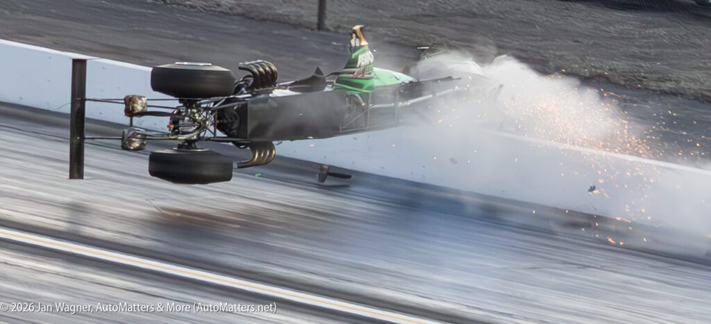 A green race car crashes sideways into a track barrier, sending sparks and debris flying.