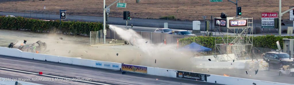 A drag racing car crashes into the side barrier, sending debris and smoke into the air at a motorsport track.