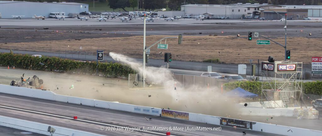 A drag race car crashes and breaks apart on a race track, with debris and smoke in the air as emergency personnel respond; airplanes and buildings are visible in the background.