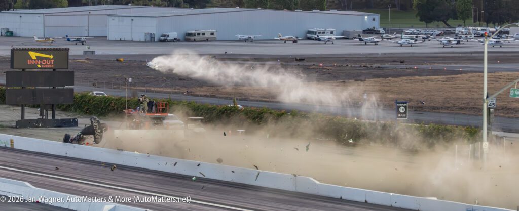 A jet-powered dragster crash sends debris and a dust cloud across a drag strip, with small planes parked in the background near an In-N-Out Burger sign.