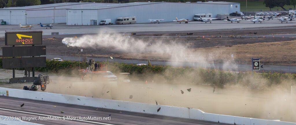 A drag car crashes, kicking up dust and debris near a racetrack; an In-N-Out Burger sign and parked planes are visible in the background.