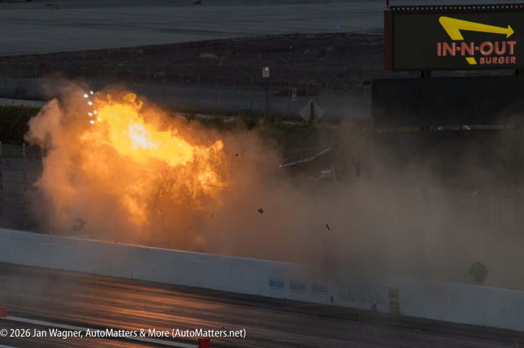 A large fireball and debris erupt from a crash on a racetrack near an In-N-Out Burger sign; the scene is filled with smoke and bright flames.