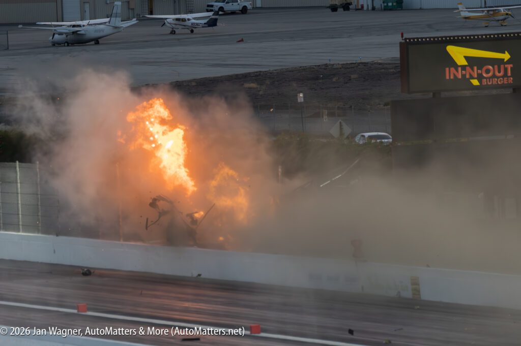 A fiery explosion with debris and heavy smoke occurs on a drag strip near an In-N-Out Burger sign and a small airport.