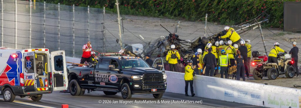 Rescue crew and emergency vehicles respond to a crash scene at a racetrack, with damaged barriers and personnel attending to the situation.