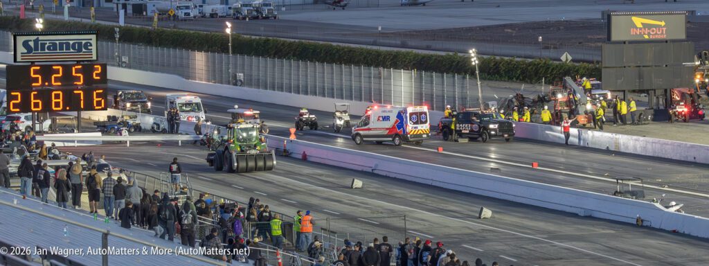 A drag racing track scene with emergency vehicles, tow trucks, and staff attending to an incident; timing board displays 5.25 seconds and 268.76 mph. Spectators watch from the stands.