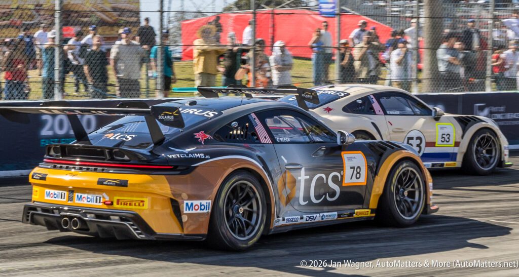 Two race cars compete on a track, with car number 78 in the foreground and car number 53 behind it; spectators and fencing are visible in the background.