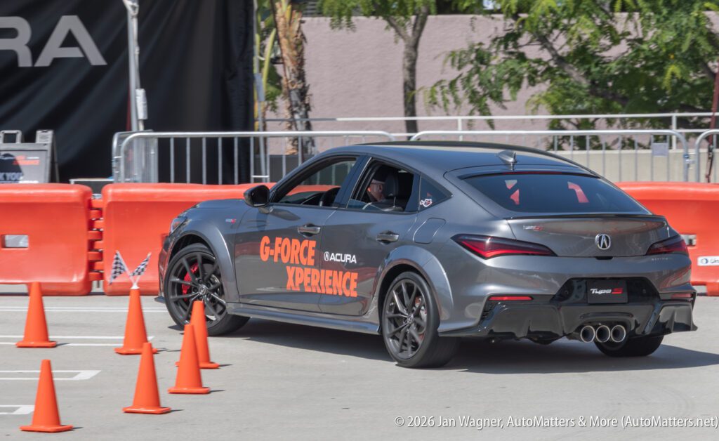 A gray Acura sedan labeled "G-Force Experience" maneuvers through orange traffic cones at an outdoor event.