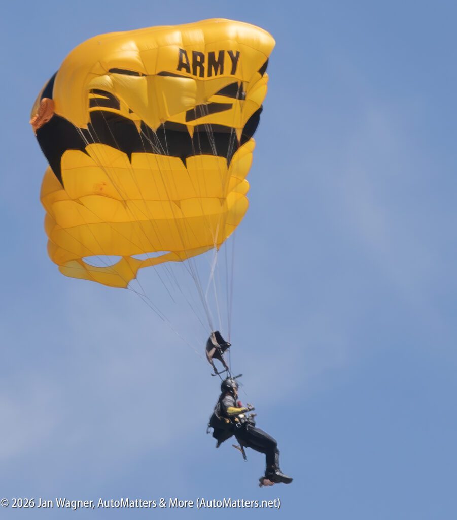 A skydiver with a yellow parachute labeled "ARMY" descends against a clear blue sky.
