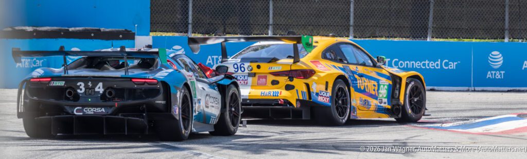 A teal and black race car and a yellow race car navigate a turn on a racetrack bordered by barriers and AT&T branding.