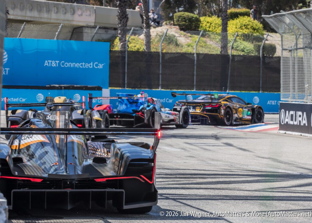 Four race cars navigate a corner on a racetrack, with barriers and sponsor signage visible in the background.