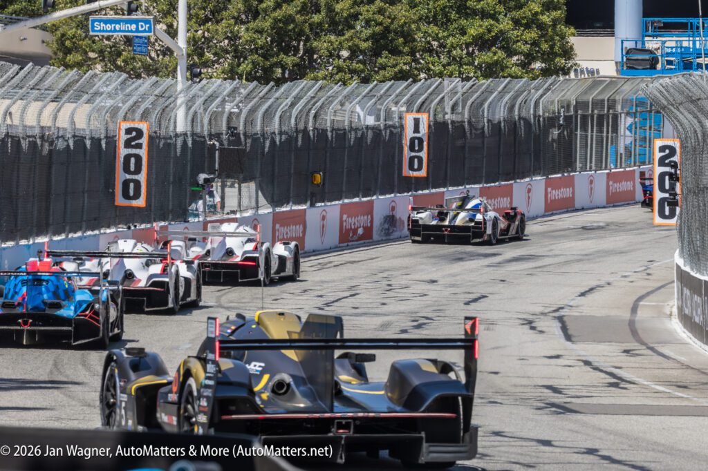 Race cars navigate a turn on a fenced street circuit, with "100" and "200" distance markers visible along the track.
