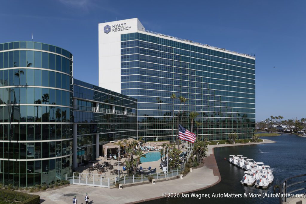 Hyatt Regency hotel building with glass exterior, outdoor pool area, American flag, and boats docked along a waterfront on a sunny day.