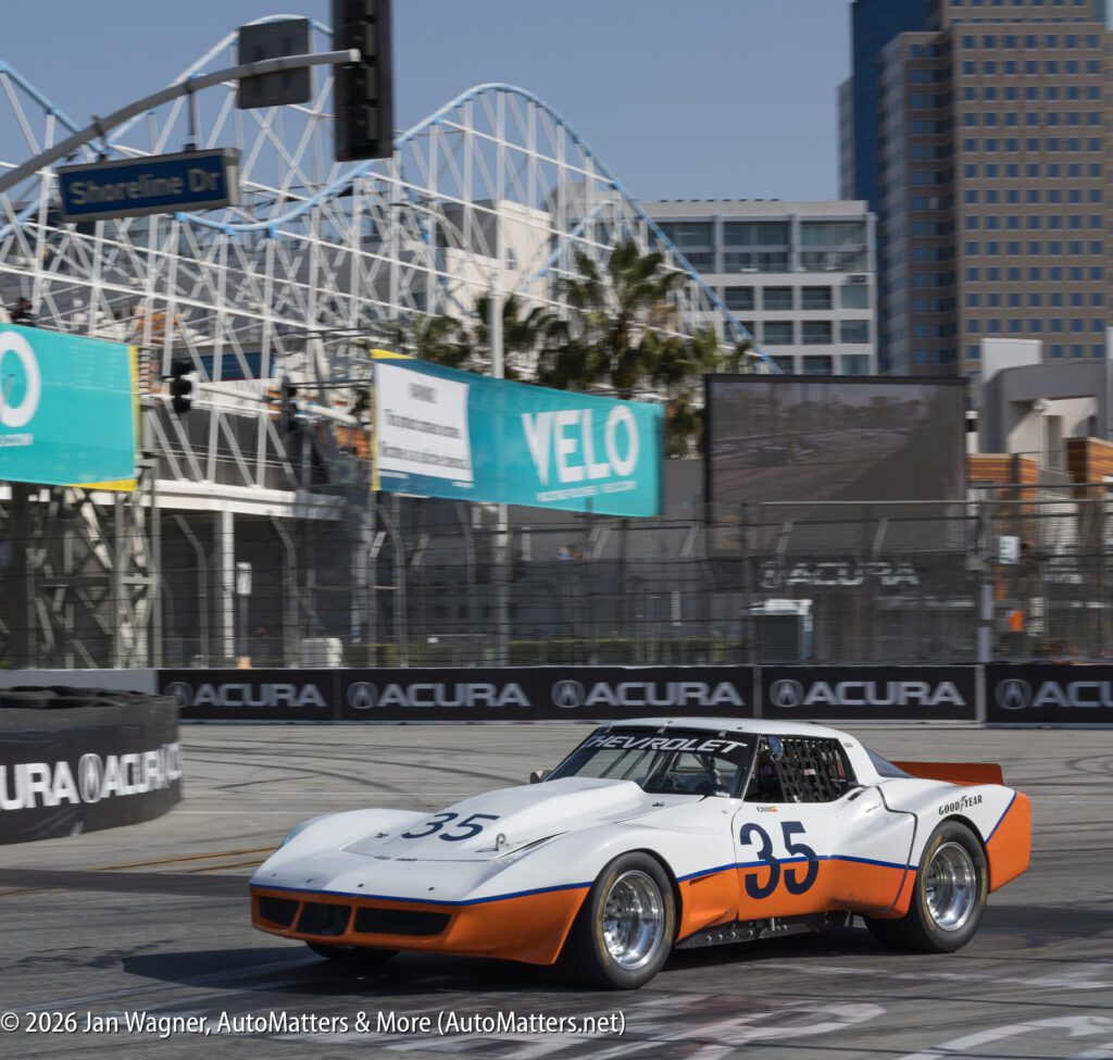 A white and orange race car with the number 35 drives on a city street circuit, with a ferris wheel and high-rise buildings in the background.