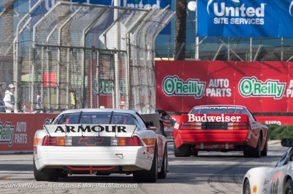 Two race cars speed around a corner on a racetrack, with visible sponsor logos such as Armour, Budweiser, O'Reilly Auto Parts, and United Site Services.