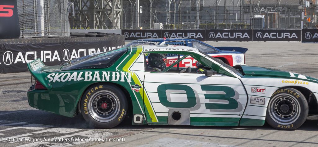 A green and white race car with the number 03 and "SKOAL BANDIT" branding is on a racetrack, with another car partially visible behind it.