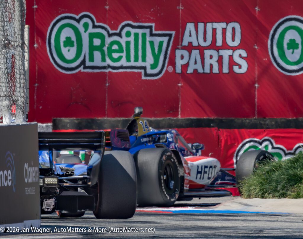 Three race cars navigate a turn on a street circuit, passing by an O'Reilly Auto Parts advertisement on a red barrier.