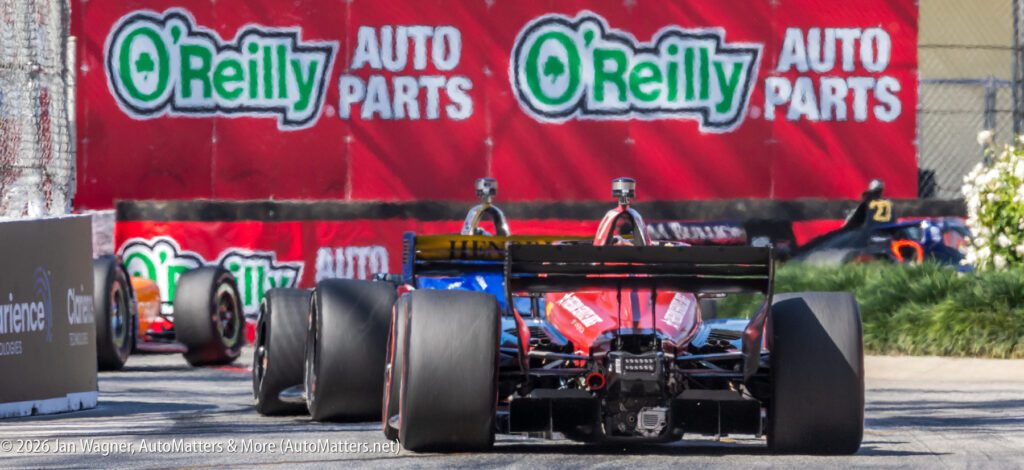 Race cars drive on a track near a barrier displaying large O'Reilly Auto Parts advertisements.