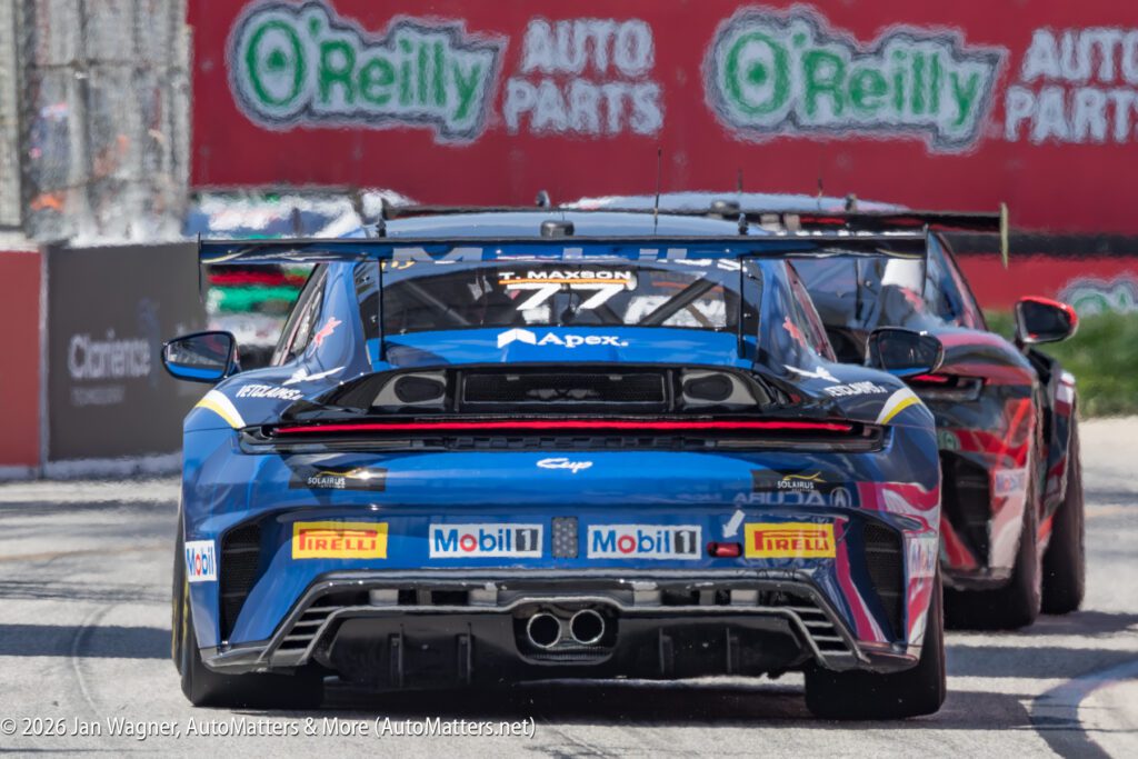 Rear view of blue and black race cars driving on a track, with O'Reilly Auto Parts ads visible in the background.