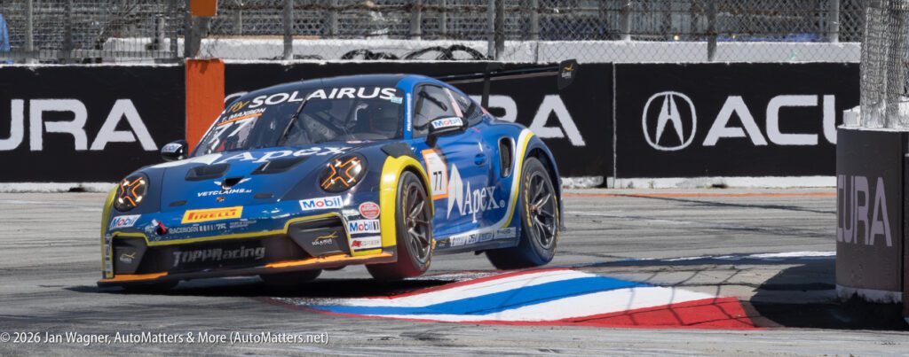 A race car with the number 4 on its windshield drives over a curb on a racetrack during a motorsport event, with Acura branding visible in the background.