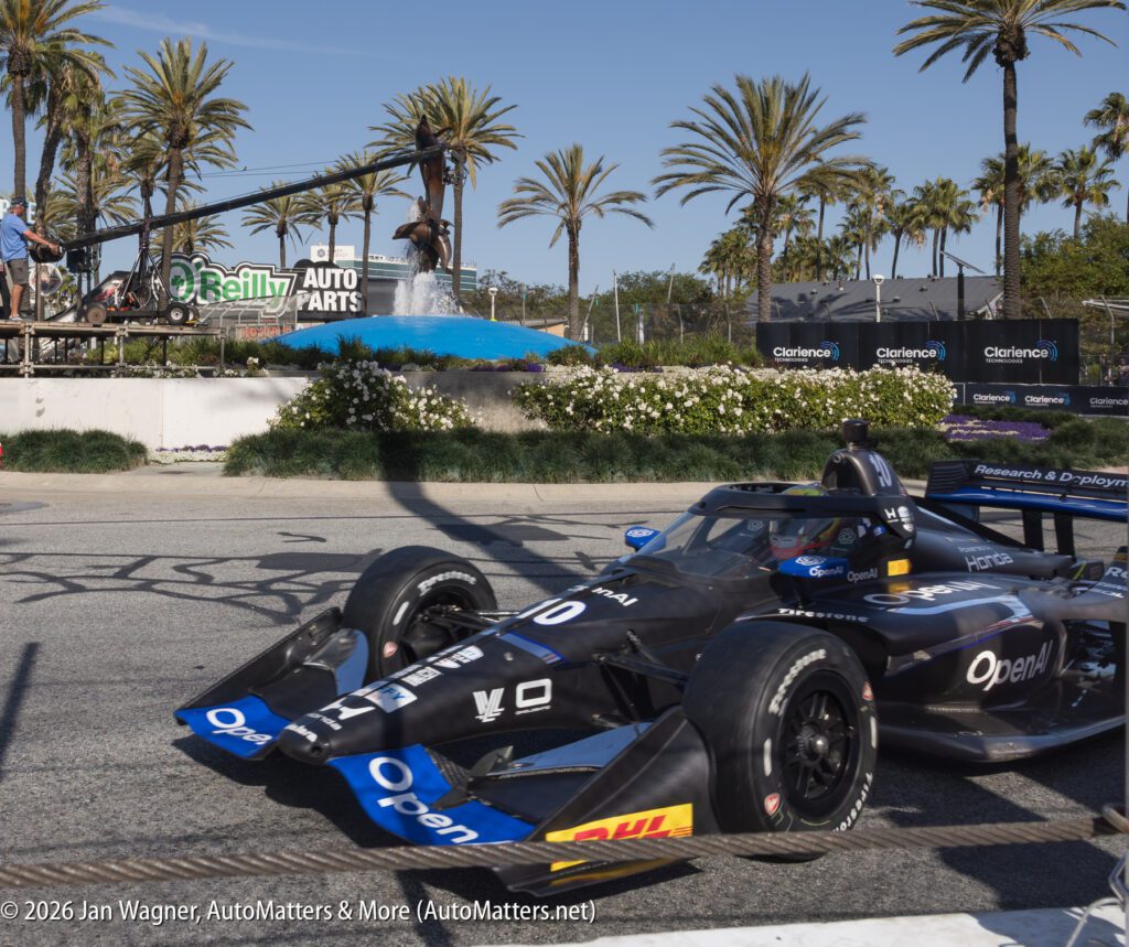 A black IndyCar with "Open" branding on the side drives on a city street circuit, palm trees and O’Reilly Auto Parts signage in the background.