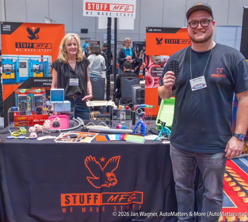 Two people stand at a trade show booth for Stuff MFG, displaying various colorful products and 3D-printed items on a table with company branding.