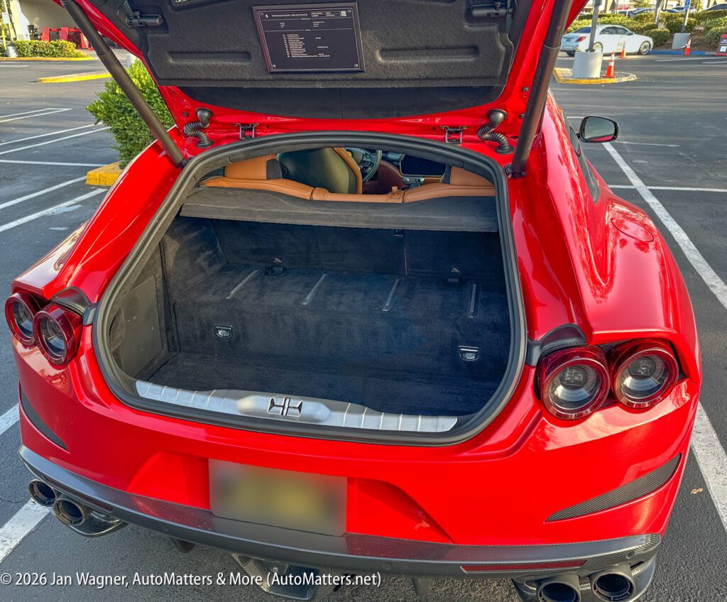 A red sports car with its trunk open, revealing a spacious black interior. The car is parked in an outdoor parking lot.