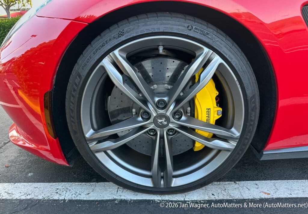 Close-up of a Ferrari wheel with a yellow brake caliper and perforated brake disc on a red car, parked on asphalt.