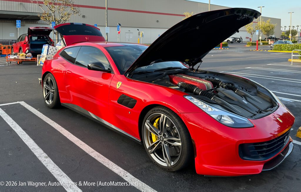 A red Ferrari with its hood open is parked in a parking lot near shopping carts and a retail store.