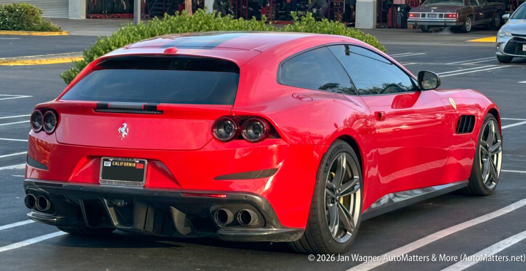A red Ferrari sports car with tinted windows is parked in a parking lot, viewed from the rear left side.